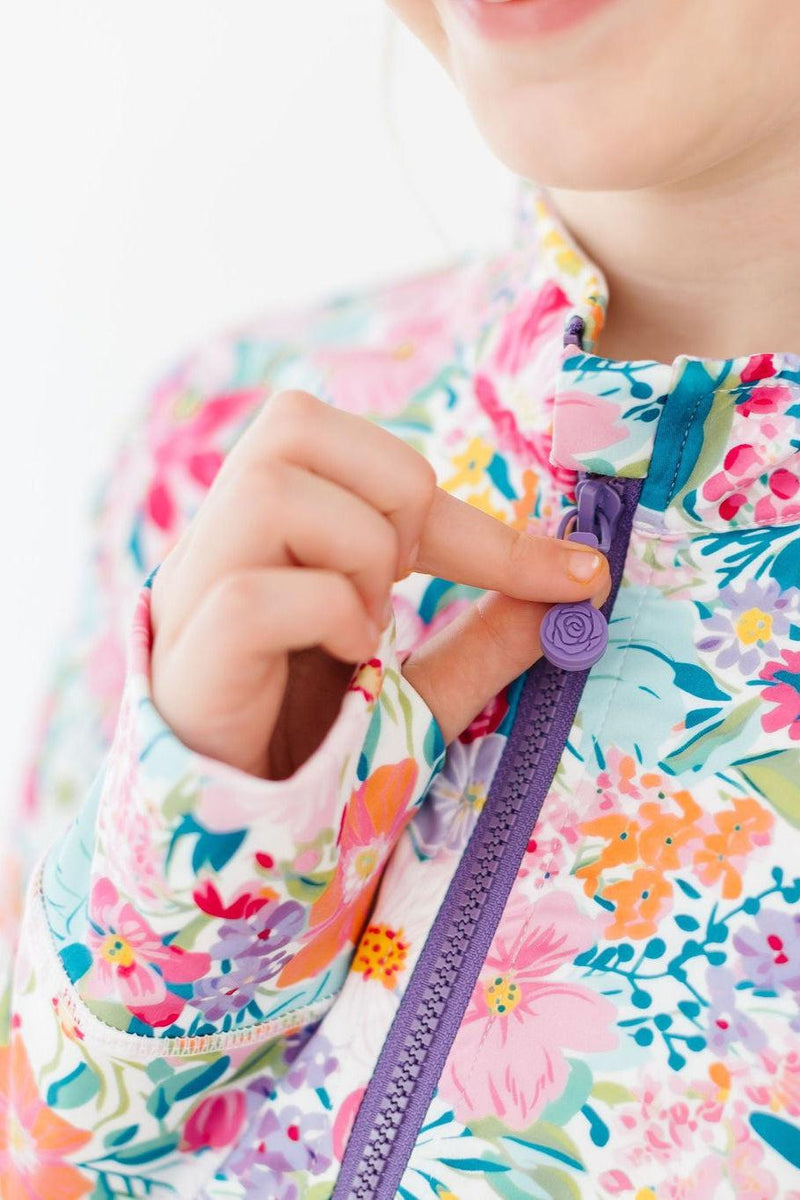 A girl smiling while adjusting the ROSE zipper of the Petal Power Full-Zip Ruffle Active Jacket, showcasing both style and functionality in a lively setting.
