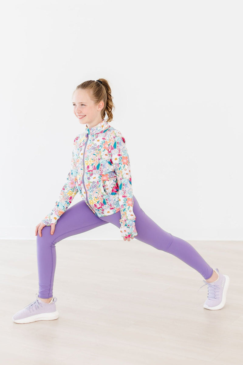 A girl in the Petal Power Full-Zip Ruffle Active Jacket captured mid-lunge, exemplifying the active lifestyle and sporty elegance.