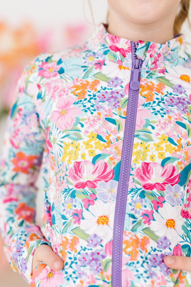 Petal Power Full-Zip Ruffle Active Jacket featuring a colorful floral pattern, worn by a happy girl with a playful expression, showcasing the stylish ROSE zipper.