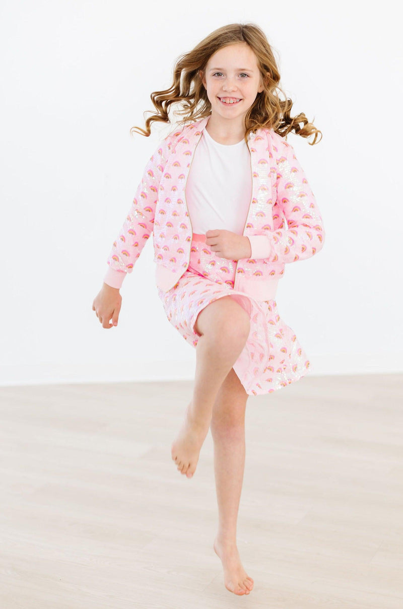 A joyful girl in mid-motion wearing the Pink Rainbow Sequin Jacket by Mila & Rose®, radiating happiness and style as she showcases her vibrant personality.