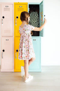Girl in Playground Princess twirl dress with a playful print beside pastel lockers.