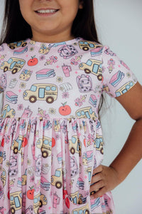 Girl in pink twirl dress with school bus and book print, short sleeves and gathered waist.