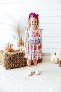 Smiling toddler in pumpkin-print Preppy Pumpkins 3/4-sleeve ruffle twirl dress with pink bow.