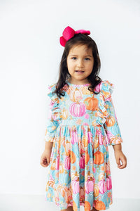Toddler girl in pumpkin-print 3/4-sleeve twirl dress with ruffles and pink bow headband.