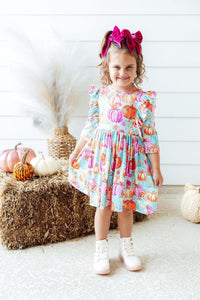 Toddler girl in Preppy Pumpkins 3/4 Sleeve Ruffle Twirl Dress with pumpkin print, pink bow headband, white boots.