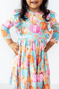 Toddler girl in the Preppy Pumpkins 3/4 Sleeve Ruffle Twirl Dress with pastel pumpkin print and ruffled sleeves.