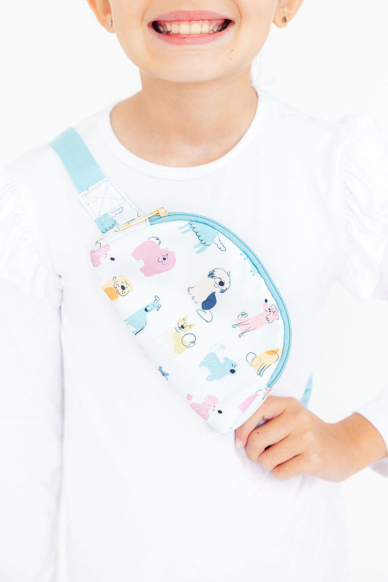 Child wearing a white crossbody belt bag with colorful cartoon dogs and blue trim for hands-free storage.