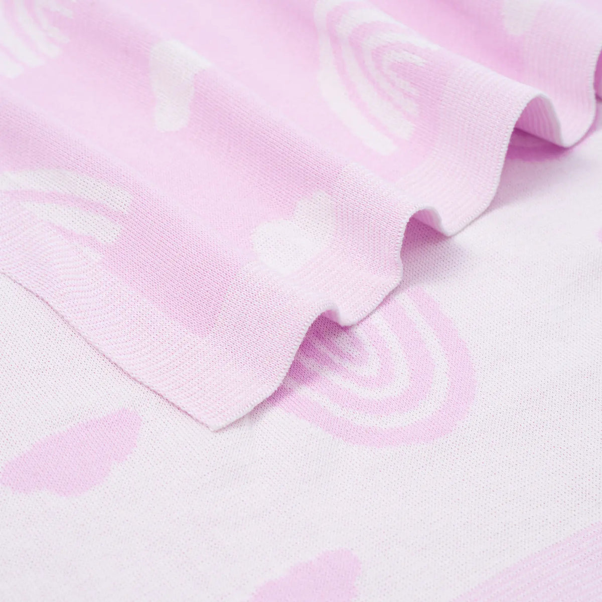 Close-up of ribbed border edge on light lilac cotton blanket highlighting soft wavy fold and fine knit texture