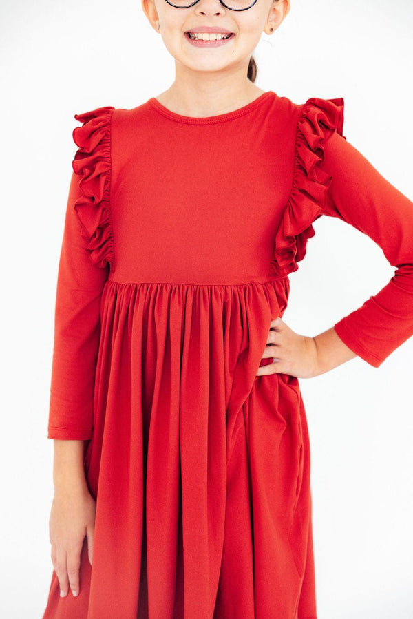 Child modeling a red long sleeve ruffle twirl dress with gathered shoulders and a flowing skirt for play and special occasions.