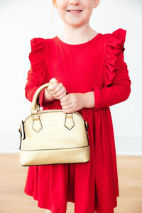 Child holding a gold purse wearing a red long sleeve ruffle twirl dress with shoulder ruffles.