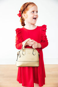 Toddler girl in red long sleeve ruffle twirl dress with braided hair and red bow, holding a gold handbag.
