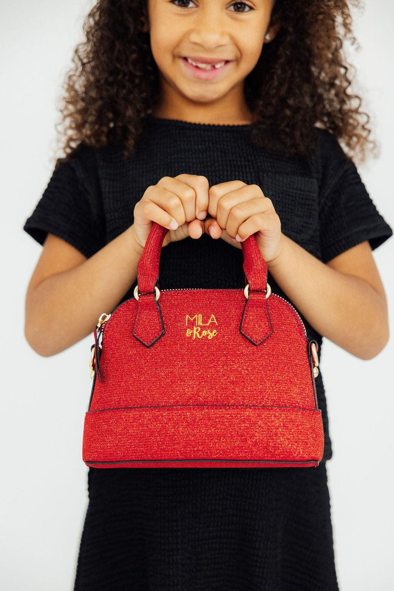 Girl holding a red shimmer crossbody purse with gold logo. Stylish handbag accessory for kids, perfect birthday or Christmas gift.