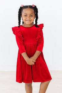 Young girl in a red velvet ruffle twirl dress with long sleeves and a full skirt for special occasions.