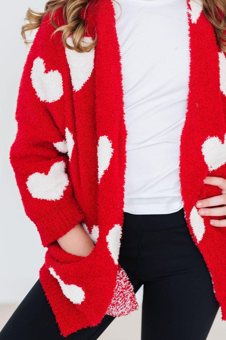 Red fuzzy heart cardigan worn open over a white tee and black leggings for a cozy, stylish look.