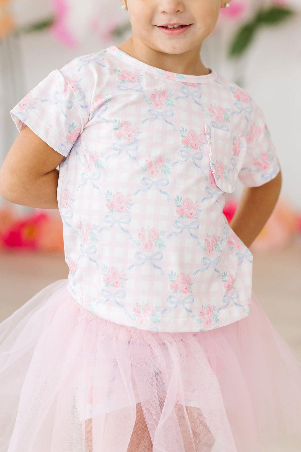Smiling girl wearing the Ribbons & Roses Ruffle Pocket Tee with a ruffled pocket, paired with a pink tulle skirt, showcasing her playful style.