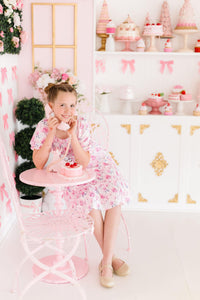 Rose Garden Smocked Ruffle Dress on a smiling girl in a pink floral outfit; stretchy smocked bodice and ruffle skirt.