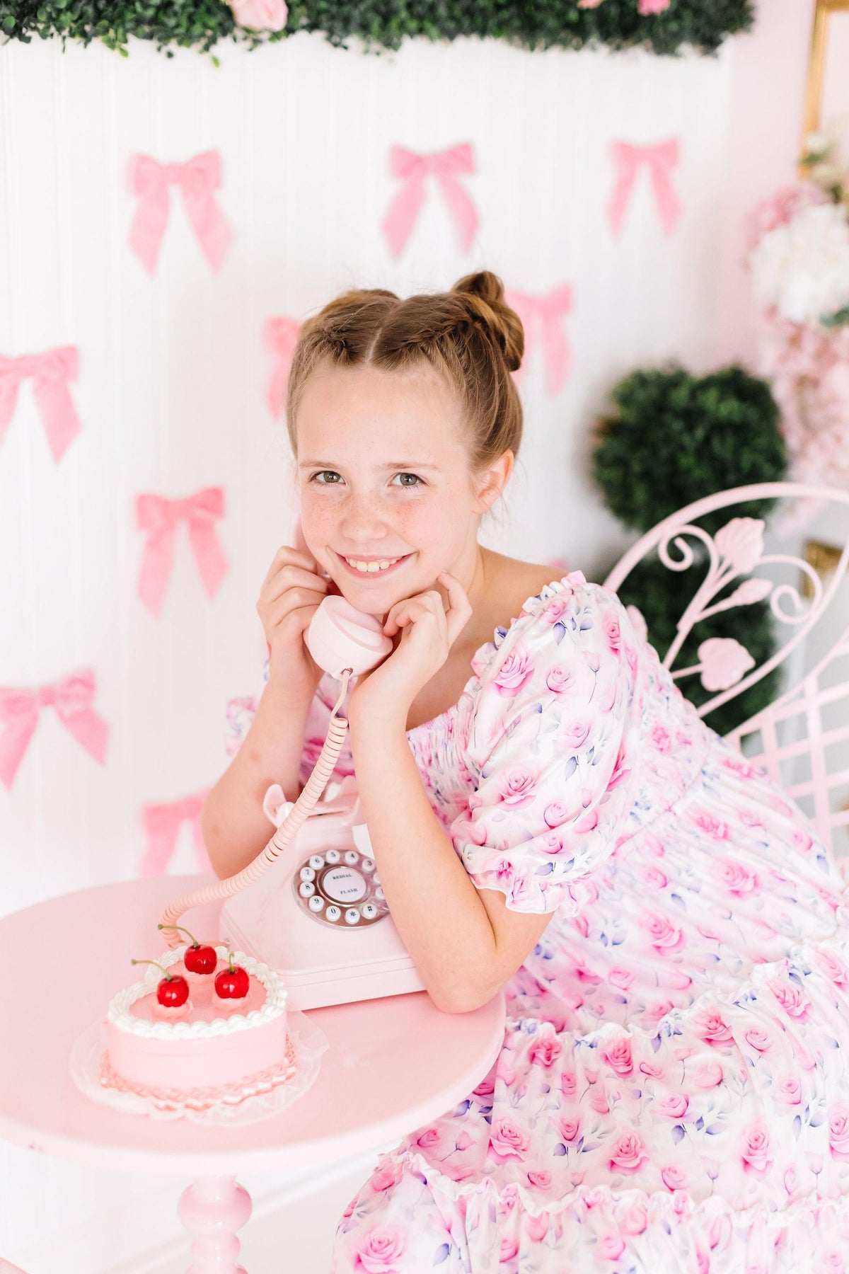 Girl in Rose Garden Smocked Ruffle Dress with pink rose print at a pastel birthday backdrop.