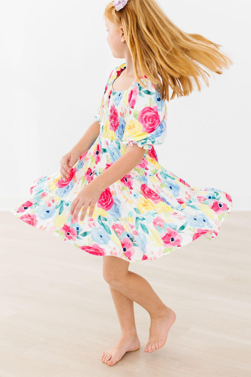 A girl joyfully twirling in the Colorful Rosie Floral Smocked Ruffle Dress, showcasing its lovely movement and vibrant design, ideal for fashion-forward girls.