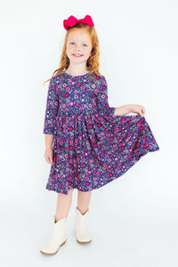 Girl wearing Flower Farm 3/4 sleeve pocket twirl dress in navy floral with scoop back and full twirl skirt.