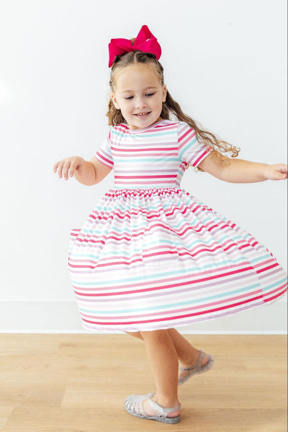 A little girl twirling in the Pastel Stripes Short Sleeve Twirl Dress, capturing the joyful spirit of this girls twirl dress.