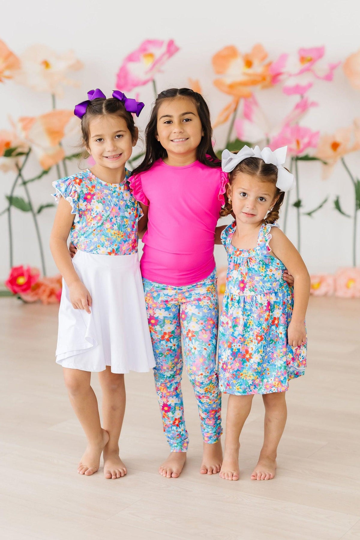 Three girls in bright floral outfits from the Preppy Floral collection with ruffles and hair bows.