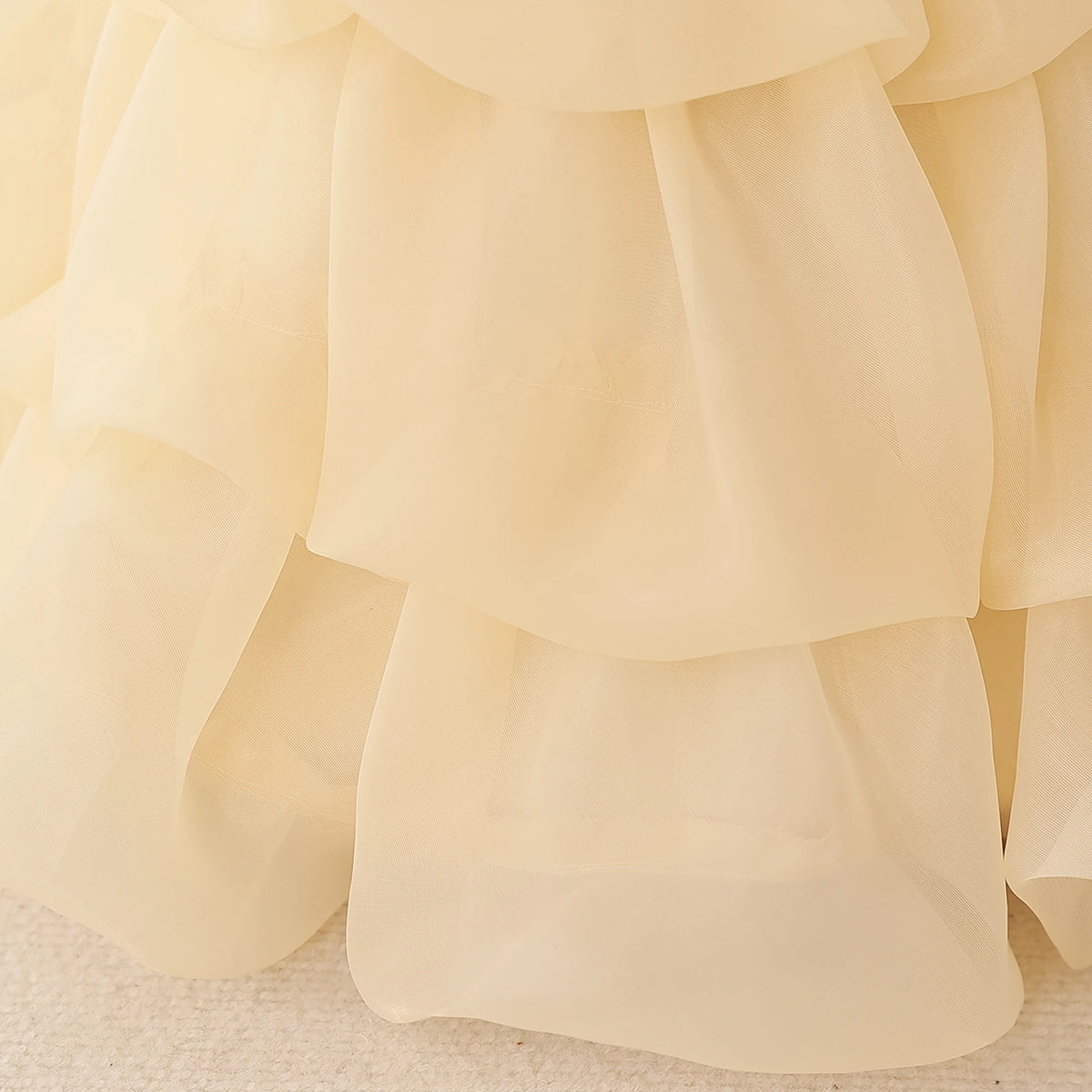 Close-up of a cream or pale yellow chiffon ruffled skirt or dress fabric, showing the layered sheer texture and soft folds.
