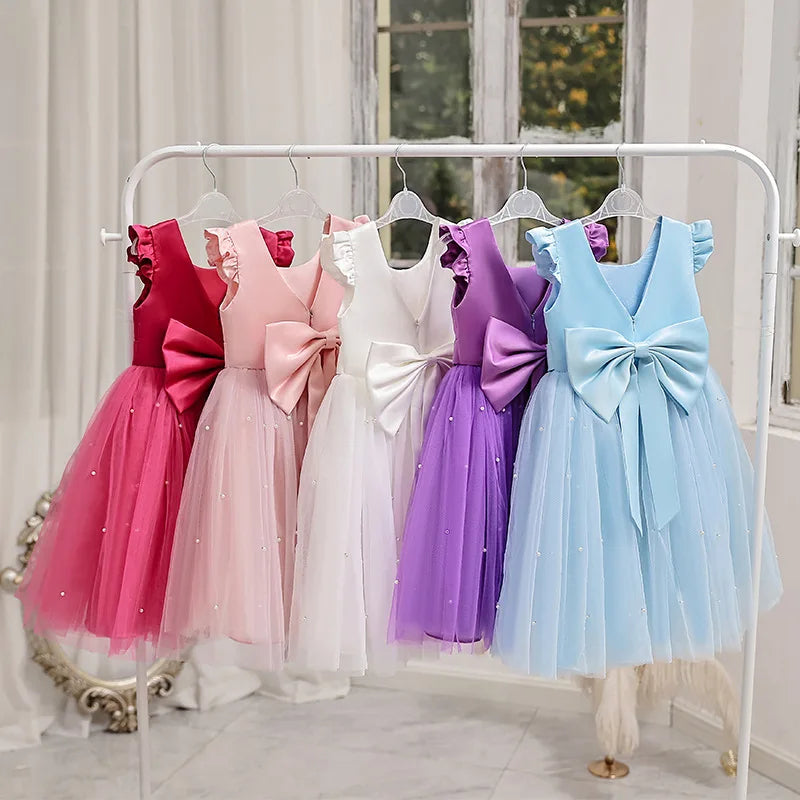 A collection of colorful 'Chantelle-Elise' V-Back Occasion Dresses on display, showcasing the elegant design with tulle skirts and oversized bows.