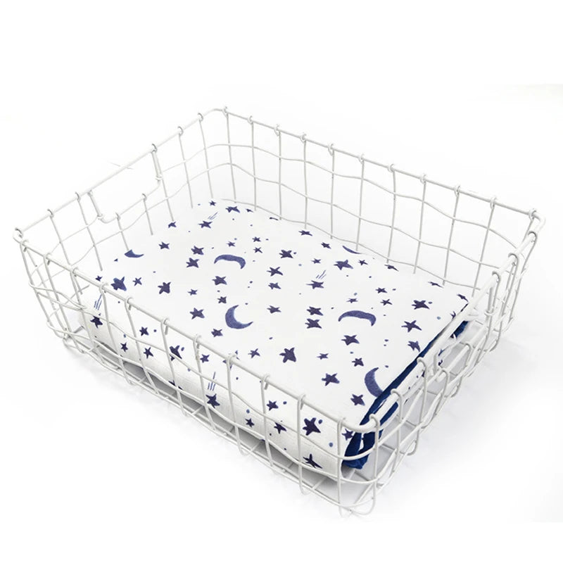 White wire basket with a 2-layer bamboo-cotton baby swaddle featuring blue moons and stars.