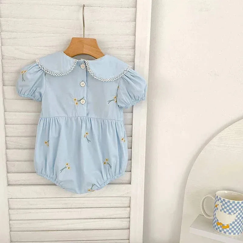 Light blue embroidered baby bubble romper with white lace collar and floral details hanging on wooden hanger
