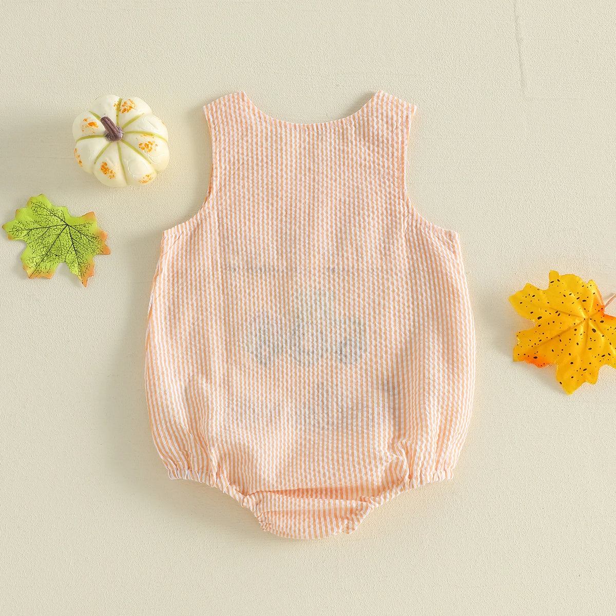 Back of orange and white seersucker baby bubble with pumpkin applique, surrounded by a mini white pumpkin and fall leaves.