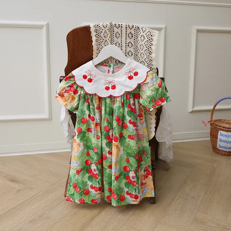 A Very Cherry Day Embroidered Dress displayed on a hanger, featuring a lovely cherry print dress design with bright colors and playful details.