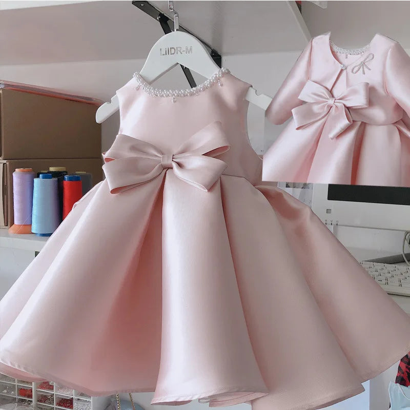 Pink satin princess dress for girls, knee-length, sleeveless with a big waist bow and beaded neckline.