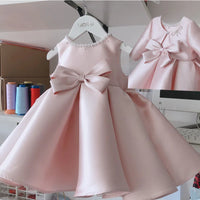 Pink satin princess dress for girls, knee-length, sleeveless with a big waist bow and beaded neckline.
