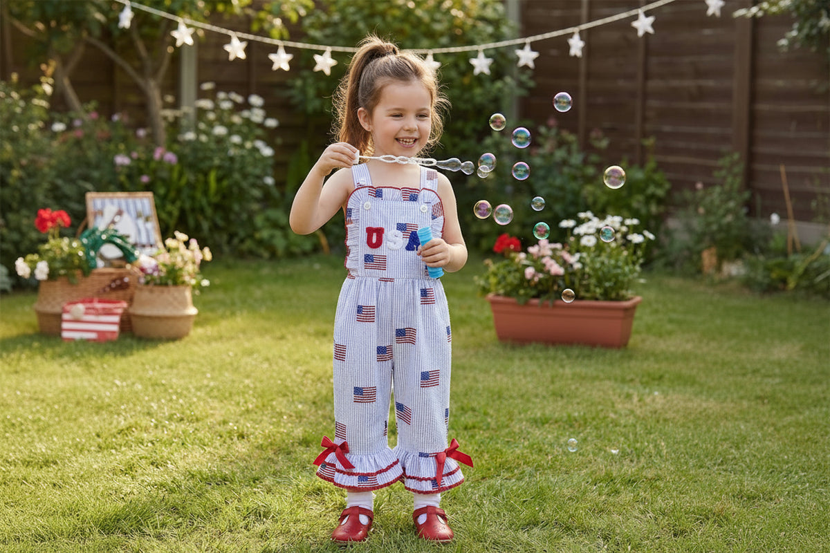 Young girl in a patriotic outfit blowing bubbles in a garden setting.