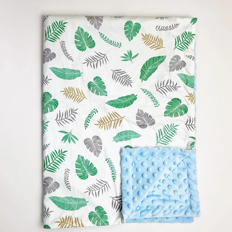 Tropical leaf print minky baby blanket with soft green, grey, and gold foliage design on white, featuring a plush light blue dotted backing for comfort.