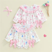 Two baby rompers with pink bows on a beige background