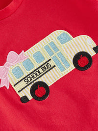 Red toddler shirt with embroidered striped bus, blue windows, black wheels with red centers, and a pink bow.
