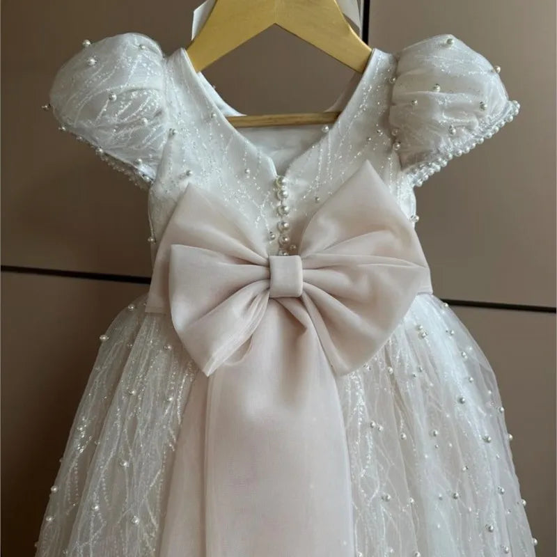 White lace dress with a large bow on a hanger against a neutral background