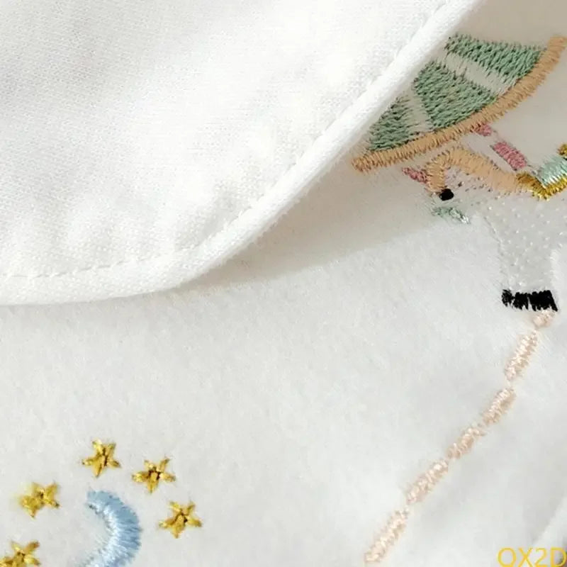 White cotton baby bib close-up featuring delicate embroidery of stars, a moon, and a carousel horse design.
