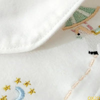 White cotton baby bib close-up featuring delicate embroidery of stars, a moon, and a carousel horse design.