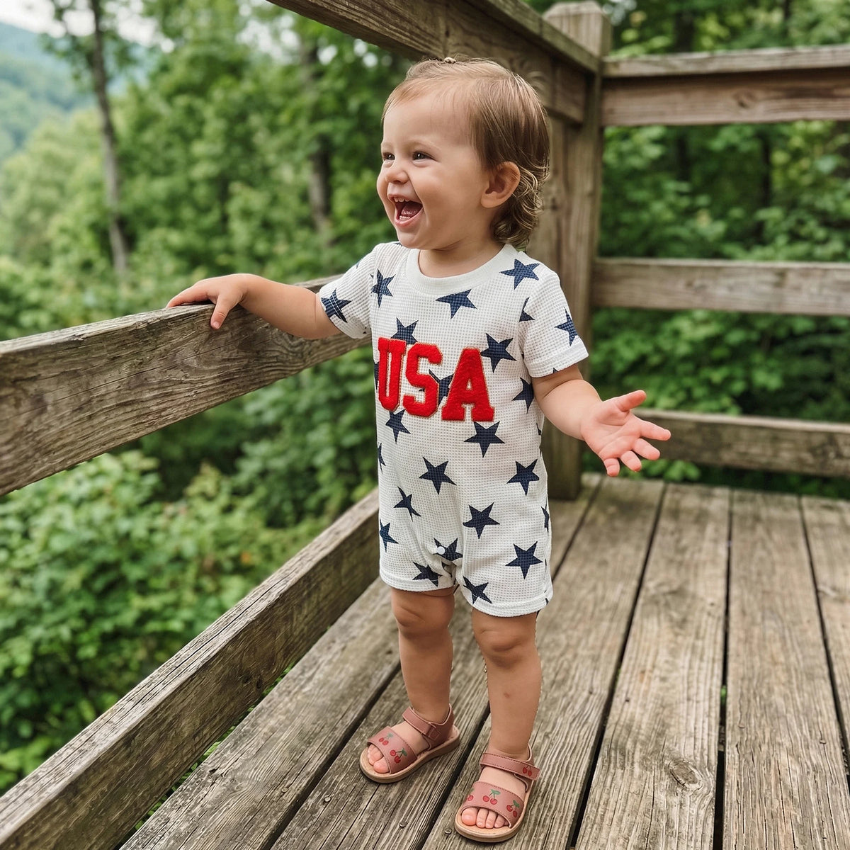 Toddler wearing Freddie USA Embroidered Patriotic Romper, enjoying a sunny day at a family BBQ. The ideal patriotic romper for toddlers for festive occasions.