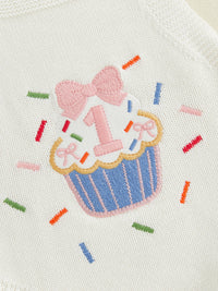 White knit romper with cupcake embroidery featuring a pink bow and colorful sprinkles.
