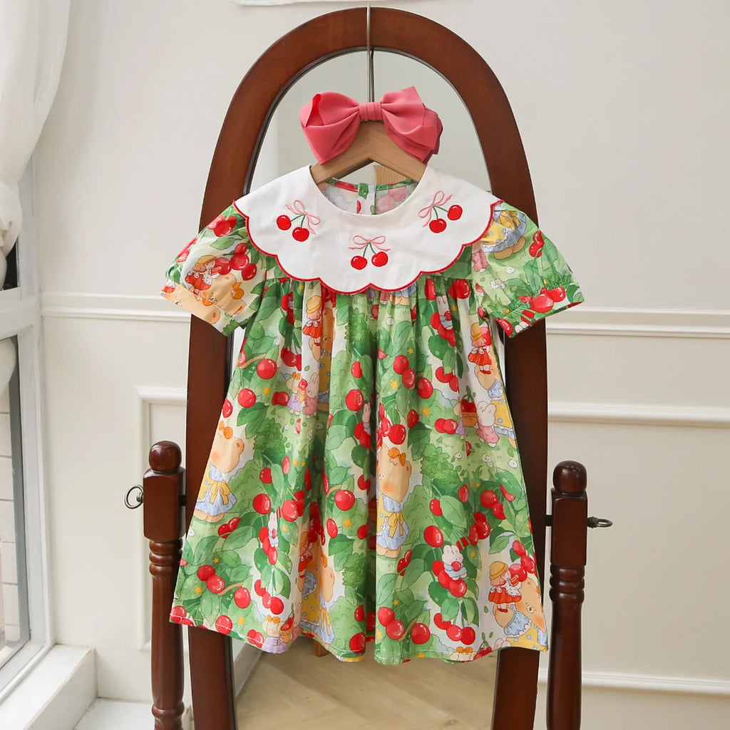 A Very Cherry Day Embroidered Dress showcasing a cute cherry print dress, featuring a vibrant cherry pattern and a scalloped collar, hanging on a mirror stand.