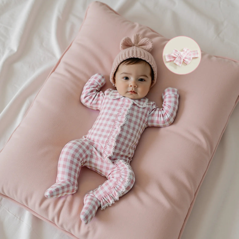 Sweet baby girl wearing the Checks and Frills Footie Set in Poinciana pink, snuggled on a soft pillow with a cute hat.