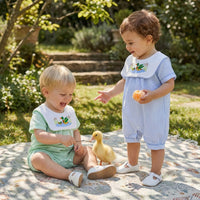 Two babies wear Little Ducky bibbed seersucker rompers in Boca Blue and Green, with embroidered mallard ducks.