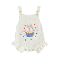 Cream knit baby romper overalls with cupcake embroidery, pink bow, colorful sprinkles, and buttoned straps.