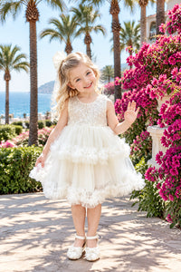 Young girl in a white dress standing outdoors with a bouquet of flowers.