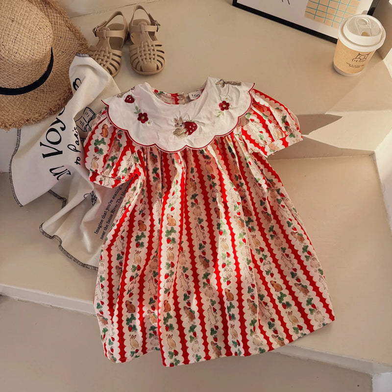 The 'Constance-Marie' classic embroidered dress for girls laid out on a surface, featuring vibrant strawberry patterns and a Peter Pan collar, ideally suited for ages 4-6 years.