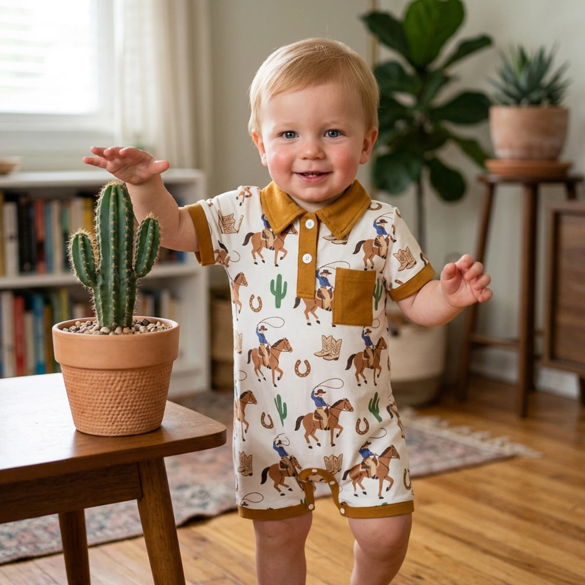 Baby boy in polo-style romper with western/fishing print, tan collar and pocket, indoors beside a cactus.