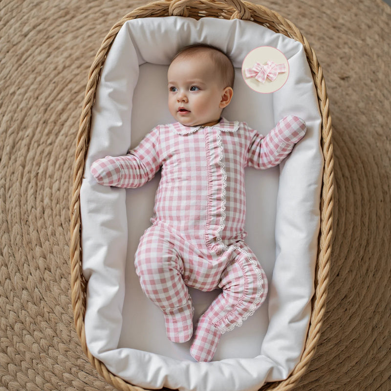 Charming baby girl exploring in the Checks and Frills Footie Set in Poinciana pink, lying on a woven surface with a matching headbow.
